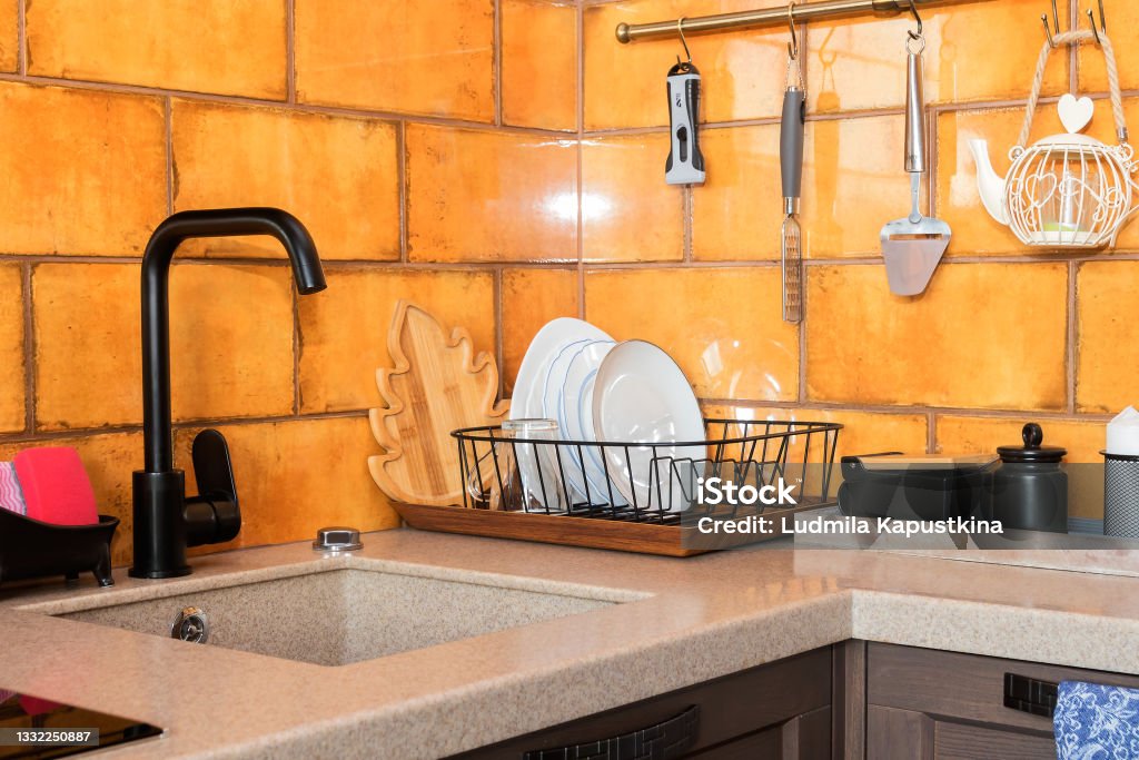 Modern kitchen design with black sink mixer and ocher ceramic tiles. Modern kitchen interior with bright ocher tiles on the walls with a fashionable stone sink. Architecture Stock Photo