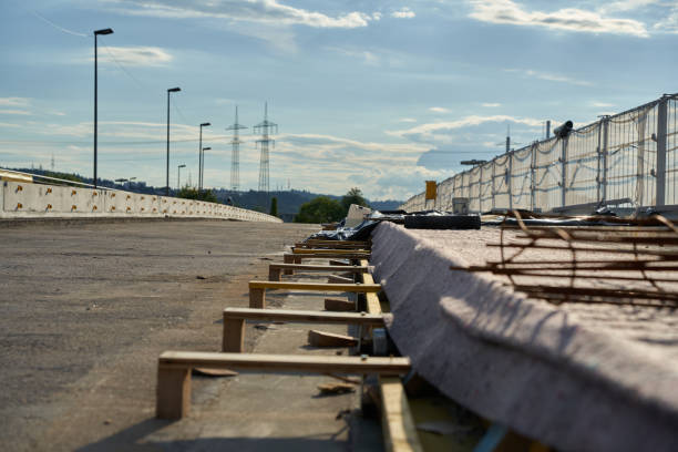 istock Bridge construction site is covered with a tarpaulin. Rusty construction steel lies on it. Iron fence secures the work. Blue cloudy sky. 1332252094