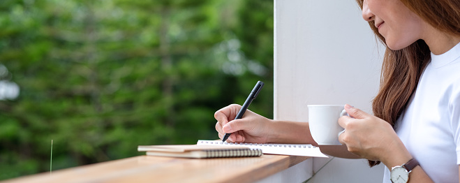 Closeup image of a beautiful young asian woman writing on a notebook in the outdoors