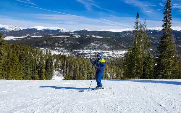 Photo of Senior skiers waving his ski pole while standing on ski slope in Colorado ski resort on sunny winter day