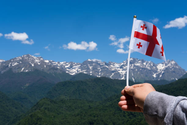 georgische flagge in der hand des menschen auf hintergrund der berge und des blauen himmels. georgische nationalflagge - svaneti stock-fotos und bilder