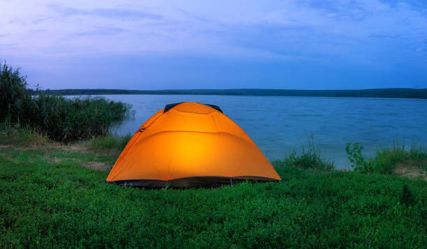 istock Orange tent illuminated from the inside by lake at dusk 1332262914