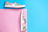 Pair of a new female's slip-ons made of floral pattern canvas on a pink-blue background. Flat lay. Copy space. Side view of shoes