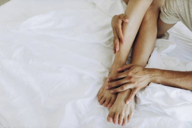 istock Thin smooth tender legs hug the hands of a man on white sheets. 1332270681