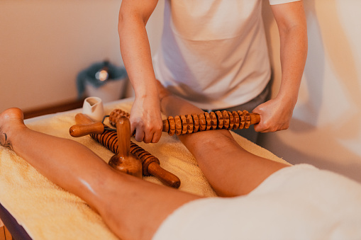 Young woman lying down on a massage table and having a maderotherapy with a rolling pin to reduce a cellulite