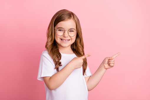 Photo of promoter small girl direct finger empty space wear eyewear white t-shirt isolated pink color background