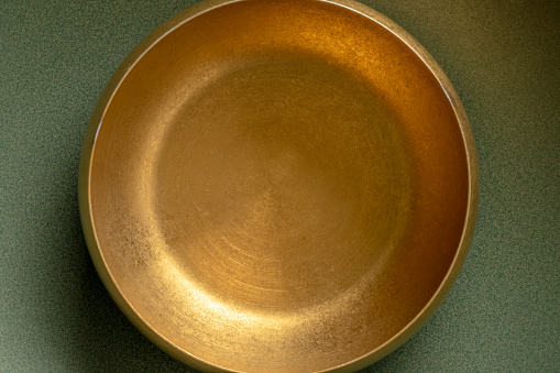 Close-up of weathered golden metal bowl on green ceramic plate with copy space.\nShot with a 35-mm full-frame 61MP Sony A7R IV with FE 90mm F2.8 Macro-lens.