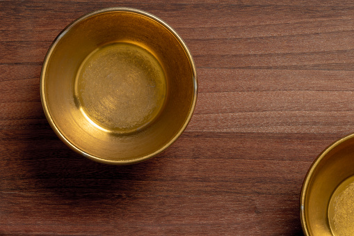 Close-up of weathered golden metal bowls on wooden table with copy space.\nShot with a 35-mm full-frame 61MP Sony A7R IV with FE 90mm F2.8 Macro-lens.
