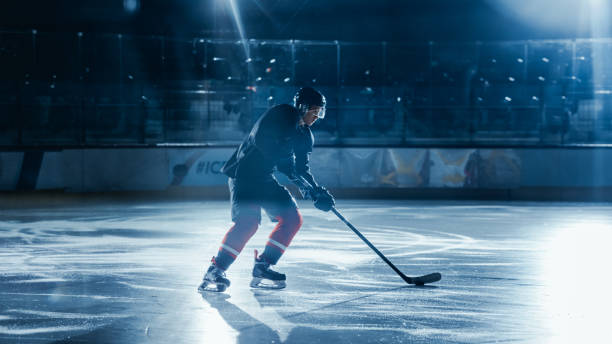 istock Ice Hockey Rink Arena: Professional Player Training Alone. Skates, Practices Shooting, Hitting, Stricking the Puck with Hockey Sticks. Determined Athlete with Desire to Win, Be Champion. 1332278057