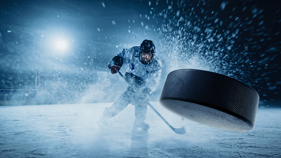 Ice Hockey Rink Arena: Jugador profesional disparando el disco con palo de hockey. Concéntrese en el disco volador 3D con efecto de movimiento de desenfoque. Tiro ancho dramático, iluminación cinemática. photo