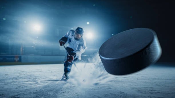 ice hockey rink arena: jogador profissional atirando o disco com bastão de hóquei. concentre-se em disco voador 3d com efeito de movimento de desfoque. tiro largo dramático, iluminação cinematográfica. - só meninos adolescentes - fotografias e filmes do acervo