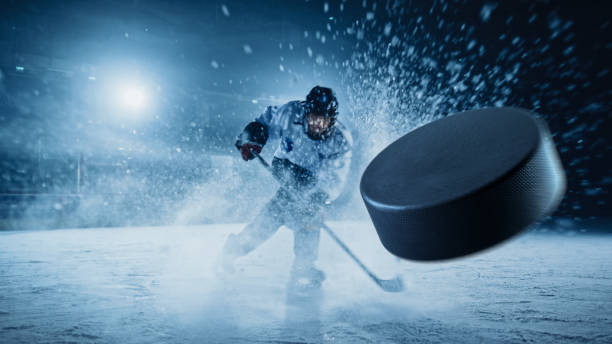 ice hockey rink arena: profesjonalny gracz strzelający do krążka kijem hokejowym. skoncentruj się na latającym krążku 3d z efektem blur motion. dramatyczne szerokie ujęcie, kinowe oświetlenie. - krążek zdjęcia i obrazy z banku zdjęć