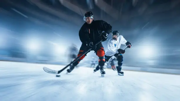 Photo of Ice Hockey Rink Arena: Professional Forward Player Masterfully Dribbles, Breaks Defense and Riding On Camera. Strong Performance Teams Play. Blurred motion Shot.