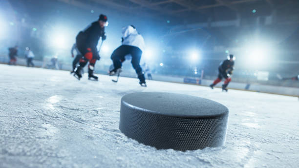 Close-up Shot with Focus on a 3D Hockey Puck on Ice Hockey Rink Arena. In the Background Blurred Professional Players From Different Teams Trying to Get the Puck. Dutch Angle Shot. Close-up Shot with Focus on a 3D Hockey Puck on Ice Hockey Rink Arena. In the Background Blurred Professional Players From Different Teams Trying to Get the Puck. Dutch Angle Shot. ice hockey stock pictures, royalty-free photos & images