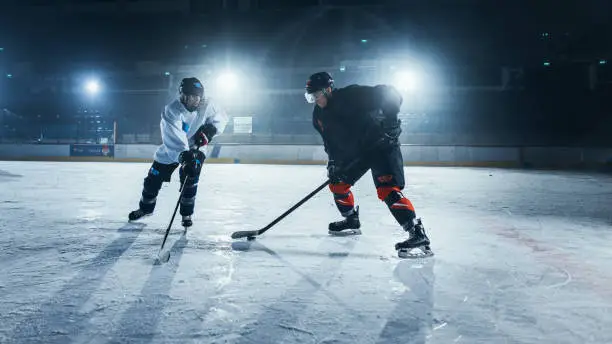 Photo of Ice Hockey Rink Arena: Two Young Players Training, Learning Stick and Puck Handling. Athletes Learn how to Dribble, Attack, Defend, Protect, Possesion, Drive the Puck.