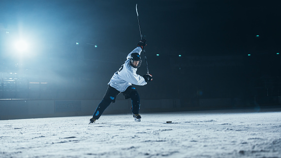 Ice Hockey Rink Arena: Professional Player Training Alone. Skates, Dribbles with Stick, Hitting the Puck. Determined Athlete with Desire to Win, Be Champion.