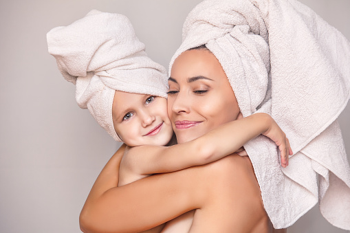 Woman young adult with daughter after shower in fresh towels hugging on isolated background