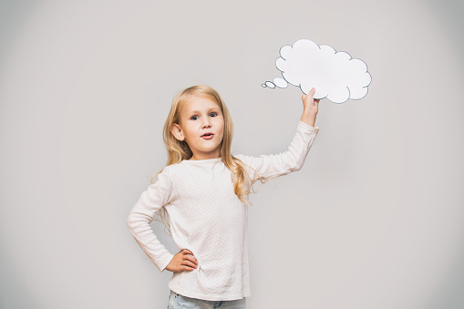 Little beautiful cute baby girl with a white cloud of thoughts in the form of a sign in the Studio on a gray background