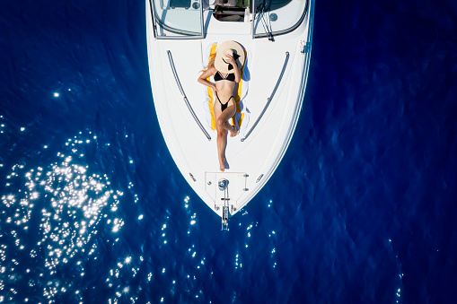 Top down view of a sexy, blonde woman in bikini taking a sunbath on a boat over blue sea during summer time