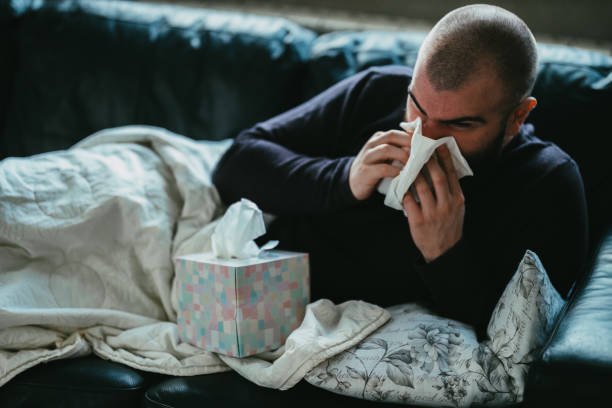 istock Sick man lying down and blowing a nose in a paper tissue 1332287645