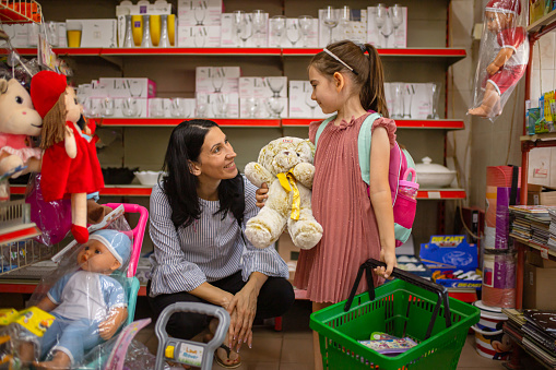 Excited preschool/school girl, with her caring mother buying her school supplies in the market-retail place, ready for her first day at school