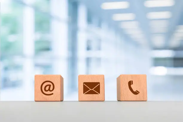 Contact us concept, wooden blocks with email, mail and telephone iconswith office background, web page contact us or e-mail marketing