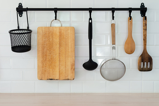 Kitchen utensils hanging on black rack and white background.