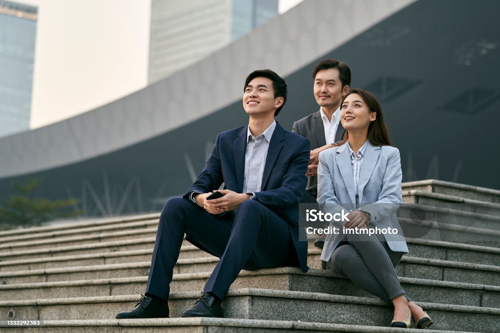 asian business people relaxing outdoors team of three asian corporate executives talking chatting relaxing outdoors Asia Stock Photo