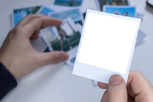 Photo of A person holds a polaroid photo in his hands against the background of other photos. Photo in hand close-up. A person looks at a photo from a polaroid.