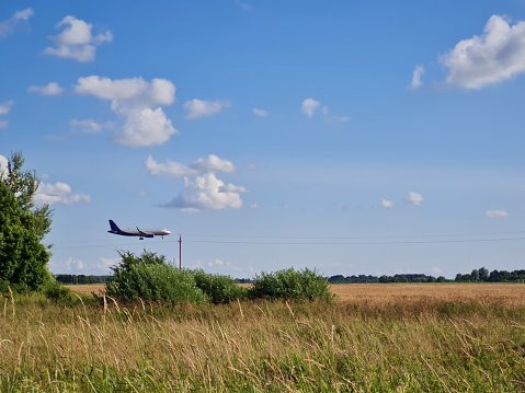 the plane is landing over a rural field on a sunny day