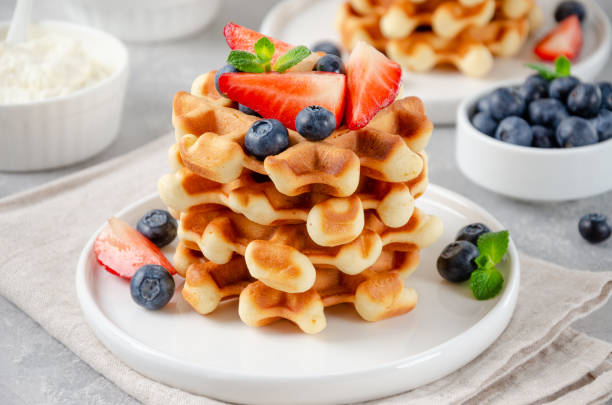istock Stack of belgian waffles with fresh strawberries, blueberries and cream on white plate on a gray concrete background. Copy space. 1332311875