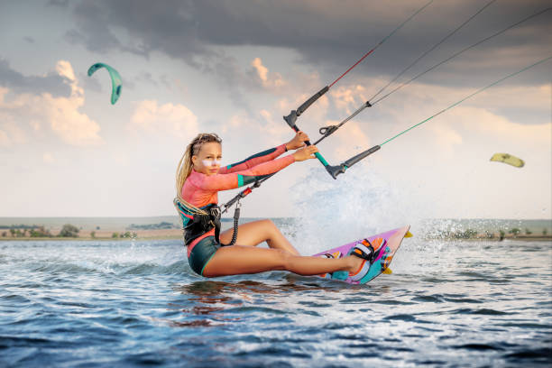 istock Front view Professional kite surfer woman rides on a board with a plank in her hands on a leman lake with sea water at evening. Water splashes and sun glare. Water sports 1332316677