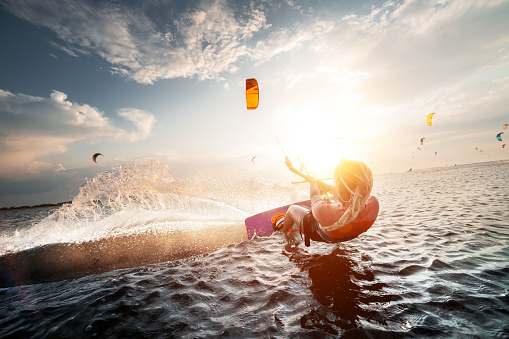 Professional kite surfer woman rides on a board with a plank in her hands on a leman lake with sea water at sunset. Water splashes and sun glare. Water sports
