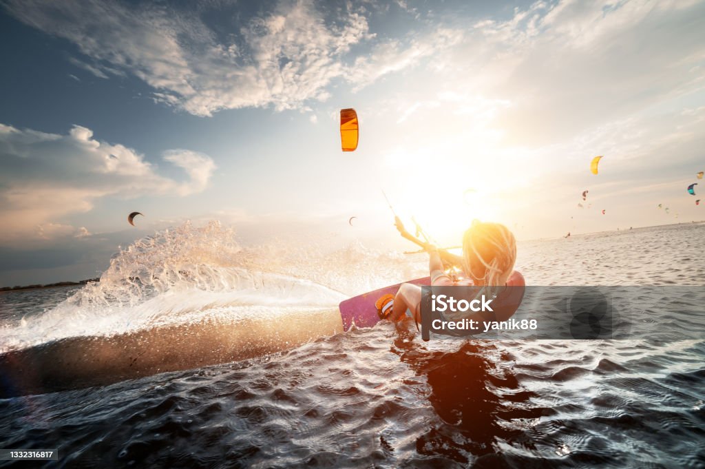 Professional kite surfer woman rides on a board with a plank in her hands on a leman lake with sea water at sunset. Water splashes and sun glare. Water sports Professional kite surfer woman rides on a board with a plank in her hands on a leman lake with sea water at sunset. Water splashes and sun glare. Water sports. Kiteboarding Stock Photo