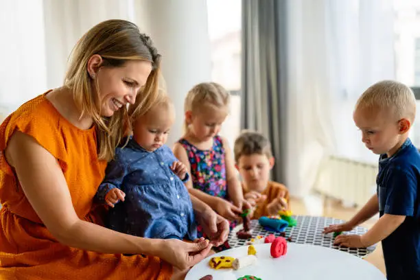 Mother or nursery teacher teaches her children to work with colorful play clay toys. Children creativity concept