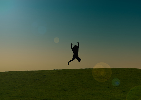 A child full of joy jumping in the air on a grass fild at dusk.