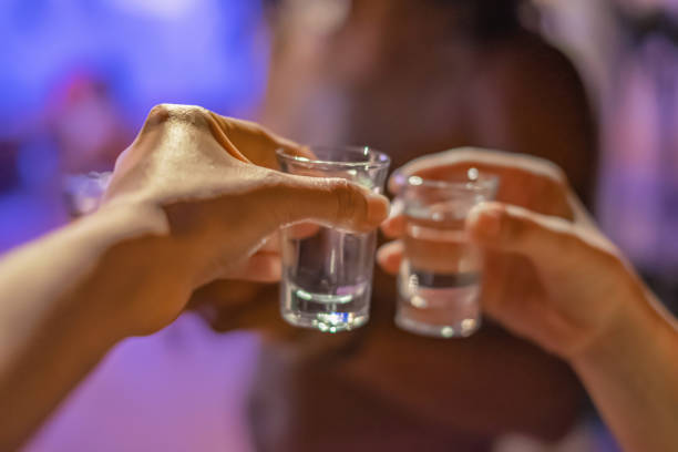 Friends Having a Birthday Celebration Toast With Tequila Shots Close-up shot of two unrecognizable hands holding a tequilla shot at a birthday celebration. They're ready for a toast. shot glass stock pictures, royalty-free photos & images