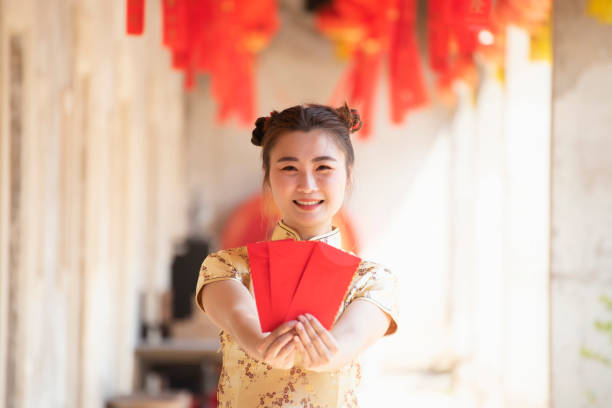 Happy asian woman in traditional chinese dress holding a red pocket with Chinese one hundred Yuan banknotes- lucky money. Tet holiday. Chinese New Year Happy asian woman in traditional chinese dress holding a red pocket with Chinese one hundred Yuan banknotes- lucky money. Tet holiday. Chinese New Year wish yuan stock pictures, royalty-free photos & images
