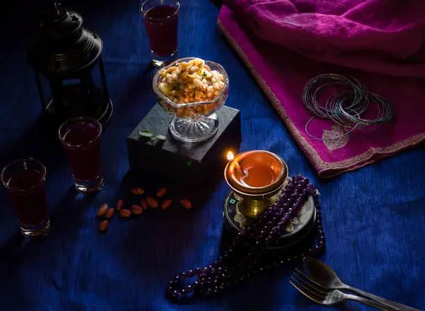 Flat Lay view of Tapioca pearl pudding,Sabudana Khichdi also called Sago Khichdi is an Indian dessert served on festivals like Diwali. Traditional,ethnic pink colored pashmina Kashmiri shawl or stole,lit up lamp, jewelry,black metal lantern,diya  on dark blue background,all add to the festive mood.