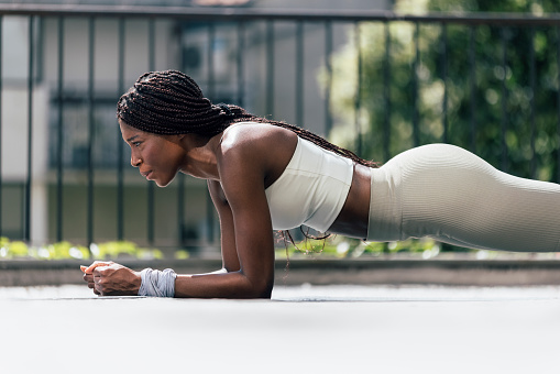 Side view of African-American woman working on abdominal muscles doing plank exercise, core workout training in the outdoor gym