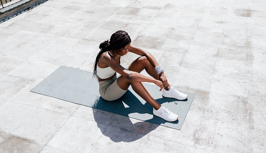 Young African-American woman in sportswear sitting on the mat tired after workout training in the outdoor gym