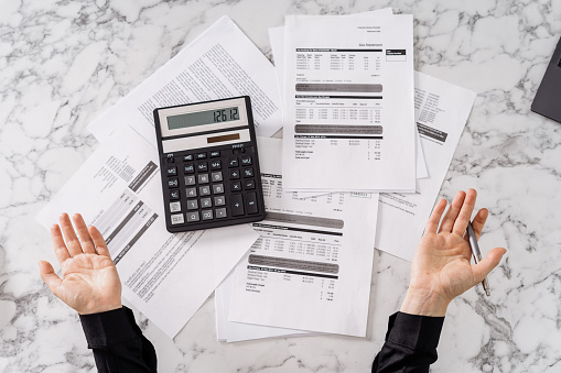 Cropped shot of person surprised by cost of monthly bills, cant believe how expensive it is, shocked after calculating all invoices, showing it with gesture while holding pen. Top view