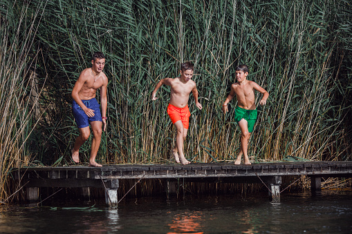 Three boys are running to leap into water. Caught in motion. They are all wet because of river water. Nature around is wonderful and river water is great for swimming and diving.