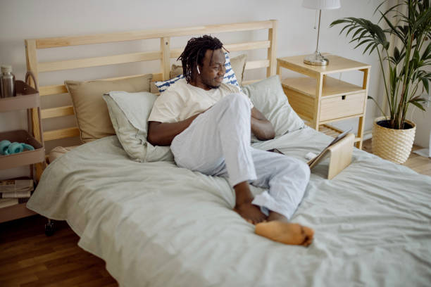 istock Black man using digital tablet making video call lying on bed at home 1332337051