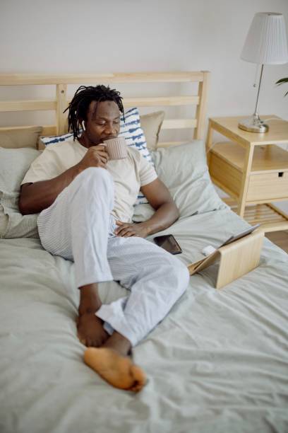 istock Black man using digital tablet making video call lying on bed at home 1332337074