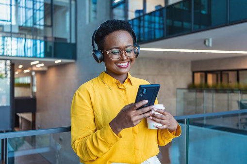 Cheerful Black Female Entrepreneur Listening Music At Workplace And Dancing, Happy African Business Lady Wearing Headphones In Office corridor
