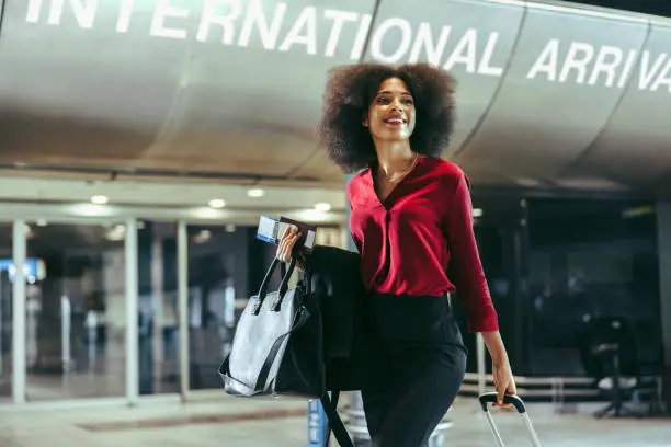 Smiling african woman with luggage walking at international airport. Happy female on international business tour.