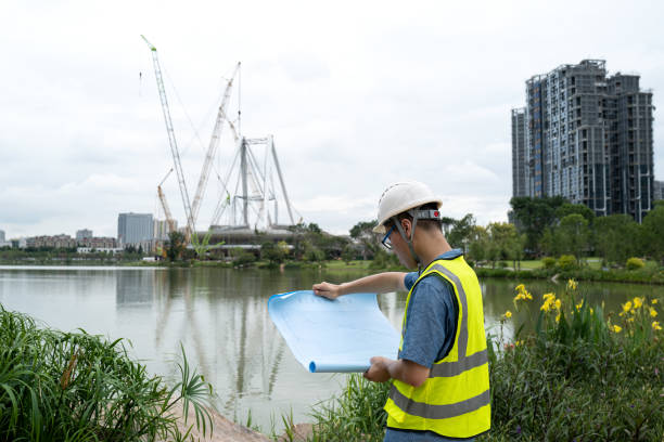 istock Asian male engineer looking at blueprints at construction site 1332339396