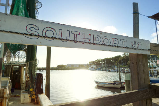 A weathered Southport , NC sign hangs at a dock in front of a fishing boat on the Cape Fear River stock photo