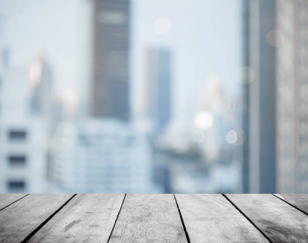 istock Panoramic empty grunge wood counter table top on blur glass window white light city bokeh background for product morning scene display montage, Abstract Blurry wide wooden desk in kitchen room rooftop. 1332346010